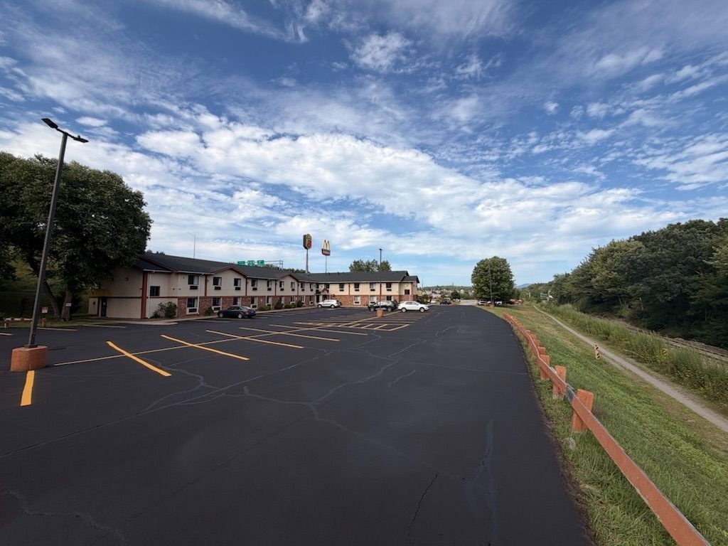 Empty parking lot beside a low building under a cloudy blue sky.