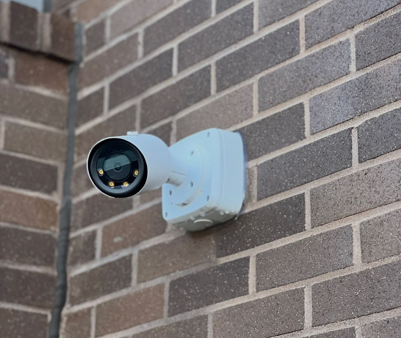 White security camera mounted on a brick wall, angled outward