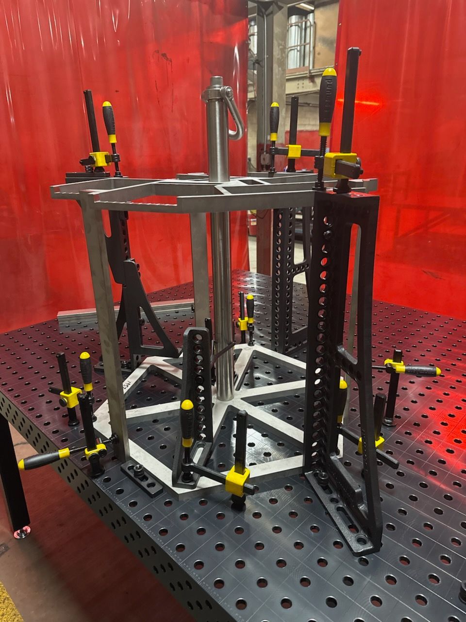 A metal frame with clamps on a black surface. A central silver pole rises from the frame.