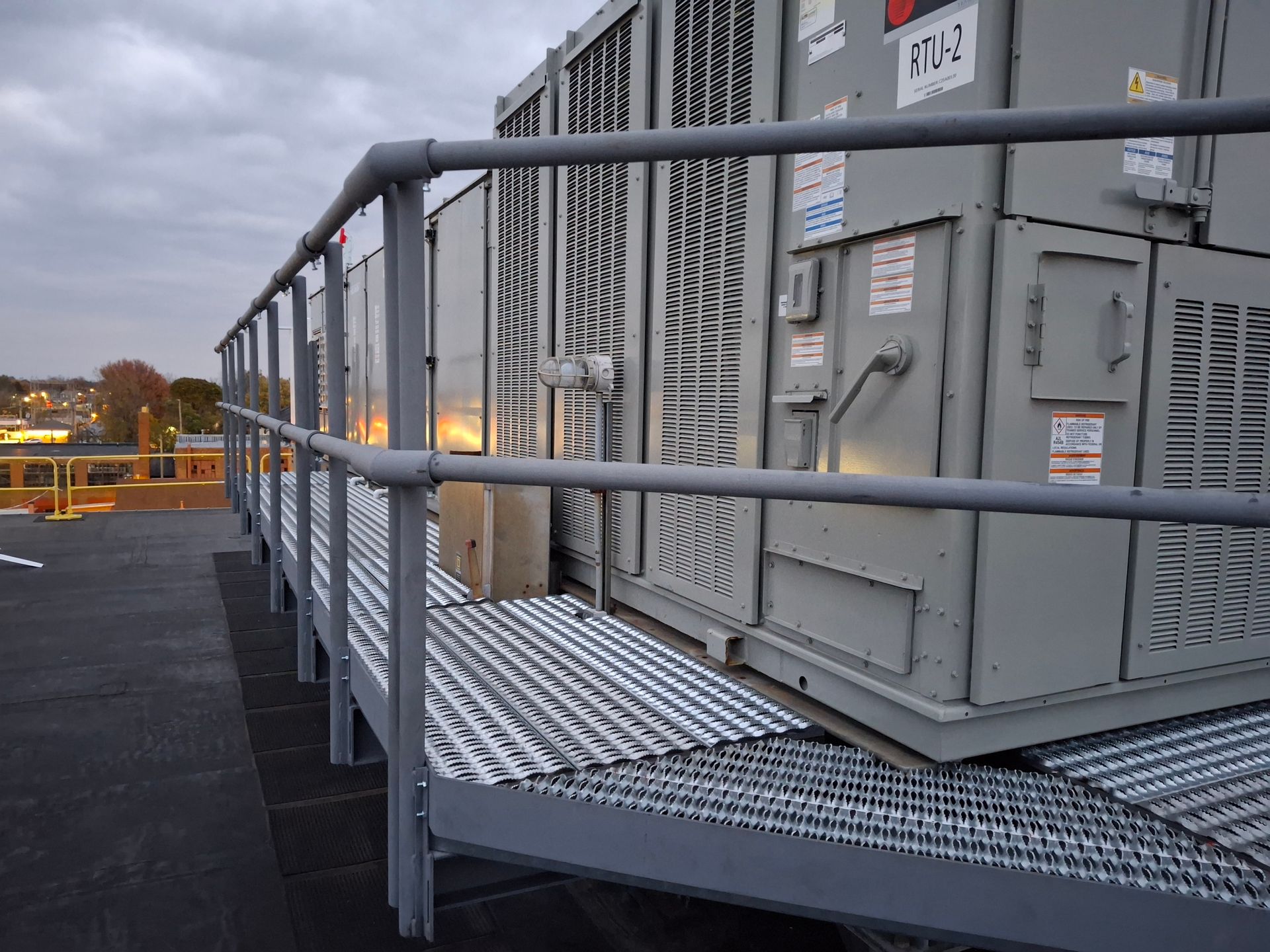 Metal railing and walkway on a rooftop with HVAC units.