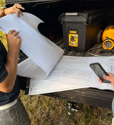People reviewing blueprints in a truck bed. A DeWalt toolbox and a flashlight are visible.