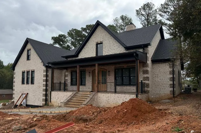 Newly constructed house with light brick exterior, black roof and trim, and porch.