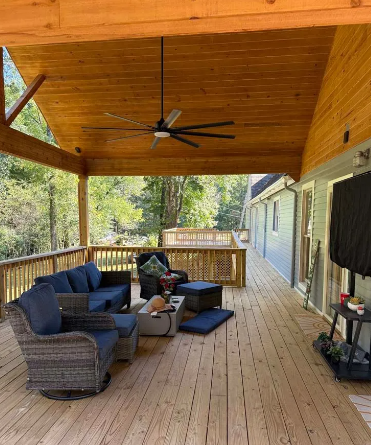 Covered wooden deck with outdoor furniture, ceiling fan, and a television.