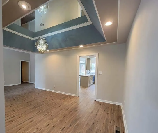 Interior view of a living room with wooden floors, neutral walls, and a recessed ceiling painted blue and beige.