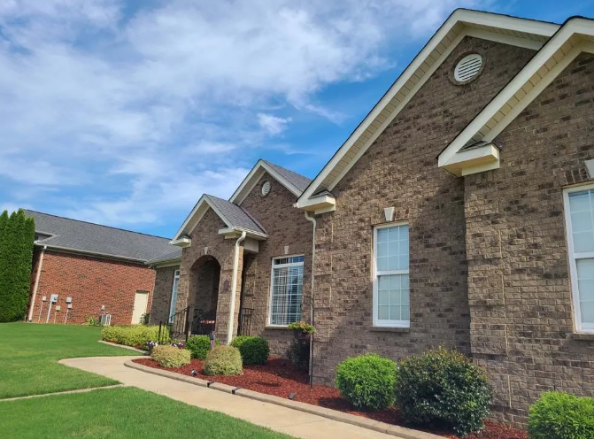 Brick house with a green lawn, red mulch, and blue sky.
