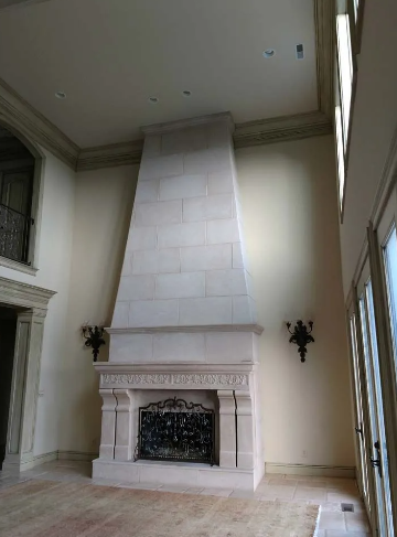 Stone fireplace in a tall room, with a black metal fire screen and sconces on the wall.