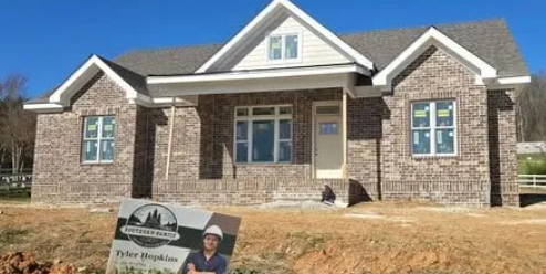 A new brick house under construction with a clear blue sky in the background. A sign is in the foreground.