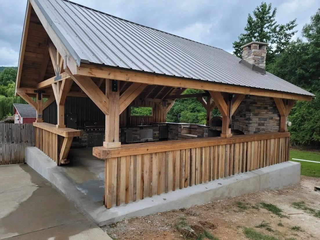 Wooden outdoor pavilion with metal roof and stone accents, on concrete foundation.