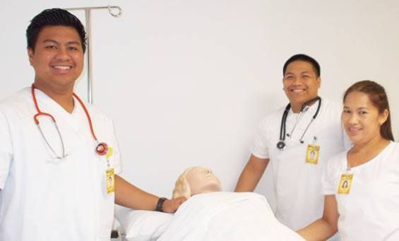 Three healthcare workers smiling, posing near a medical dummy in a white room.