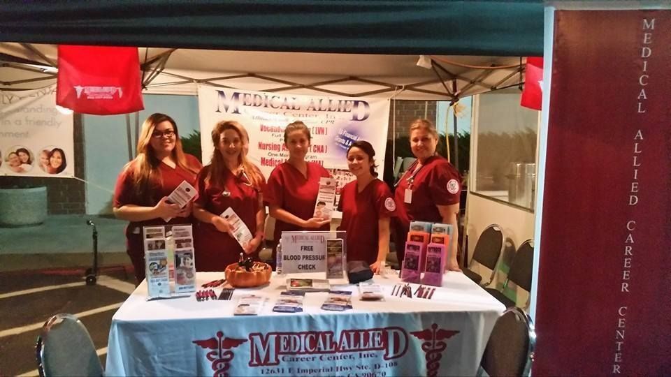 Medical Allied Career Center booth: Five women in maroon scrubs at a table with brochures.