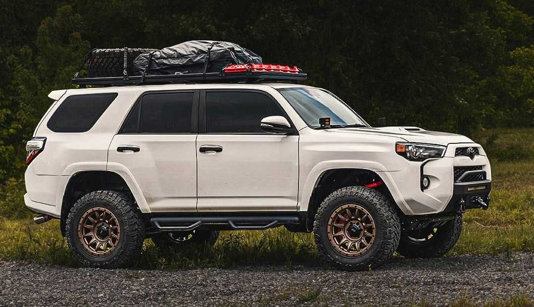 White Toyota 4Runner with off-road modifications, roof rack, and accessories parked on a gravel road in a natural setting.