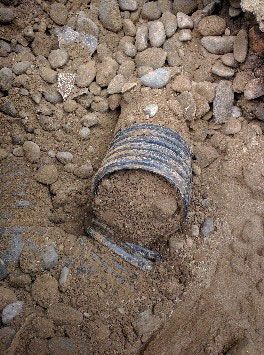 A pipe is laying in the dirt surrounded by rocks.