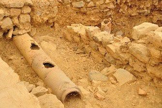 A pipe is laying in the dirt next to a stone wall.