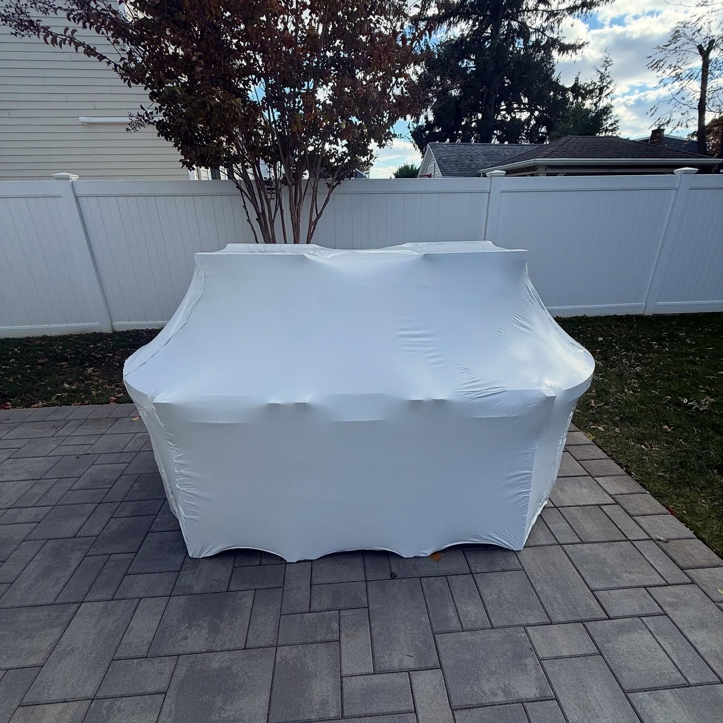 White, form-fitting table cover on a rectangular table outdoors, set on a brick patio.