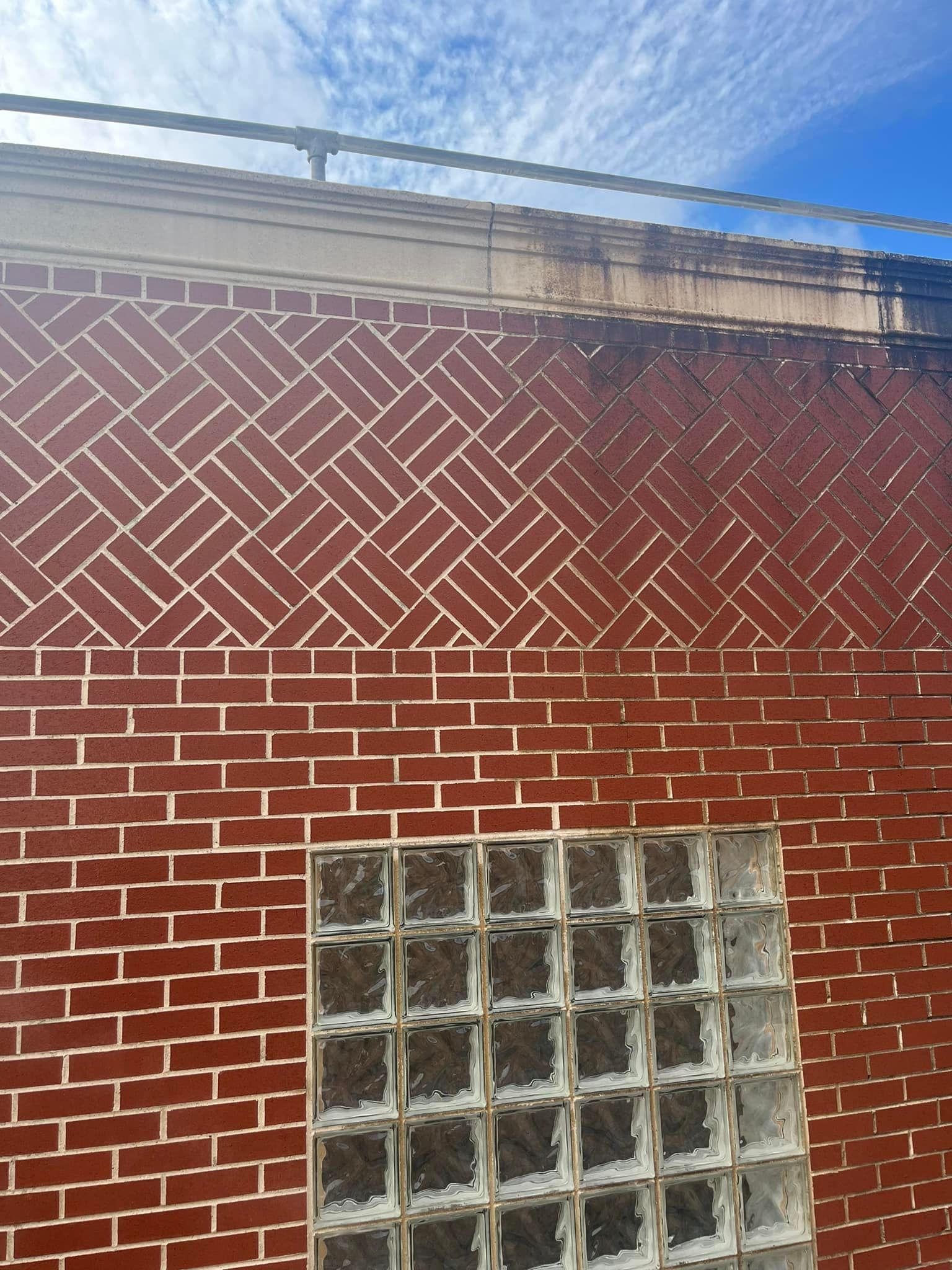 Red brick building with a patterned upper section, glass block window, and cloudy blue sky.
