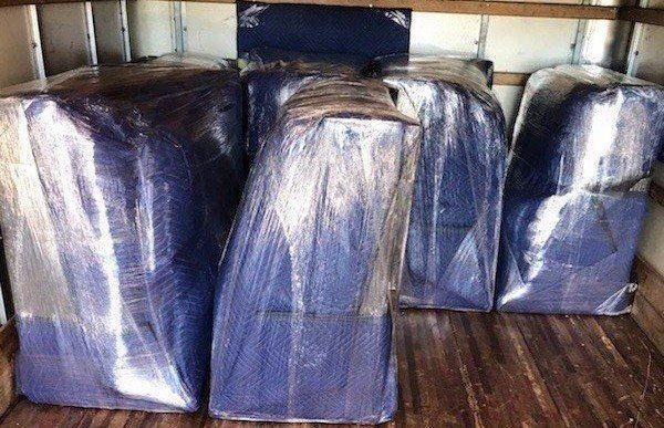 Several blue furniture pieces wrapped in clear plastic on a hardwood floor