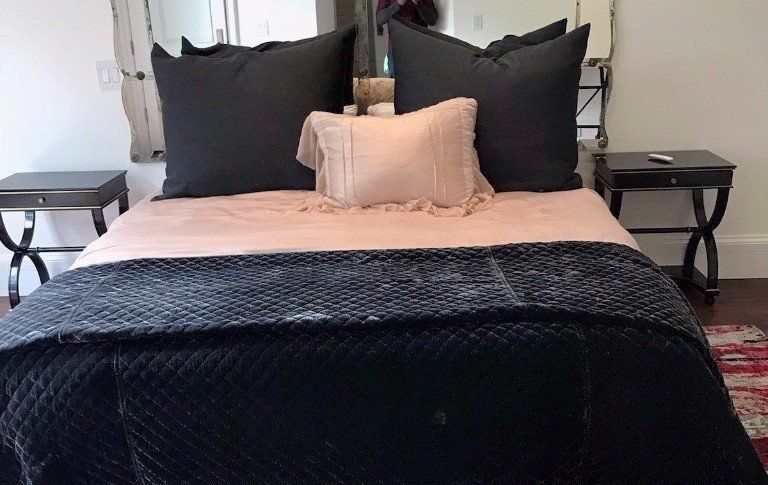 A neatly made bed with black pillows, a beige blanket, and a black throw in a bedroom.