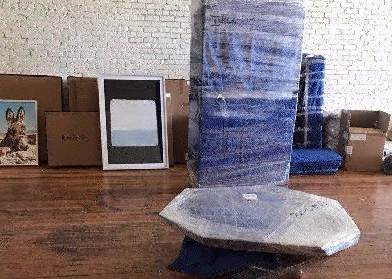 Wrapped furniture in a room with a brick wall and wooden floor, including a table and stacked items.
