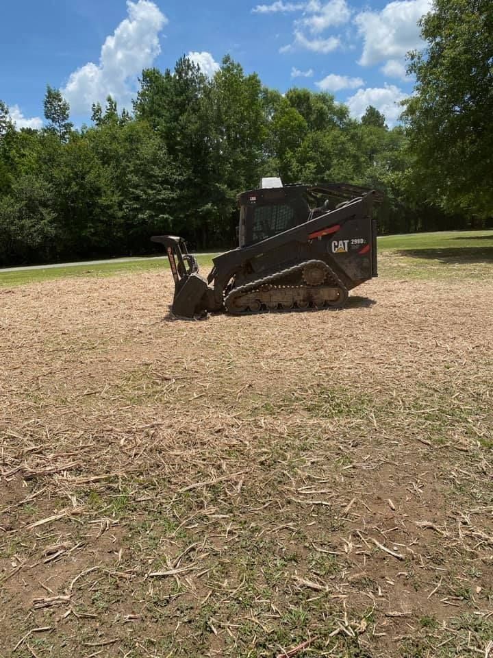 A black CAT track loader on a cleared patch of land, with trees in the background.
