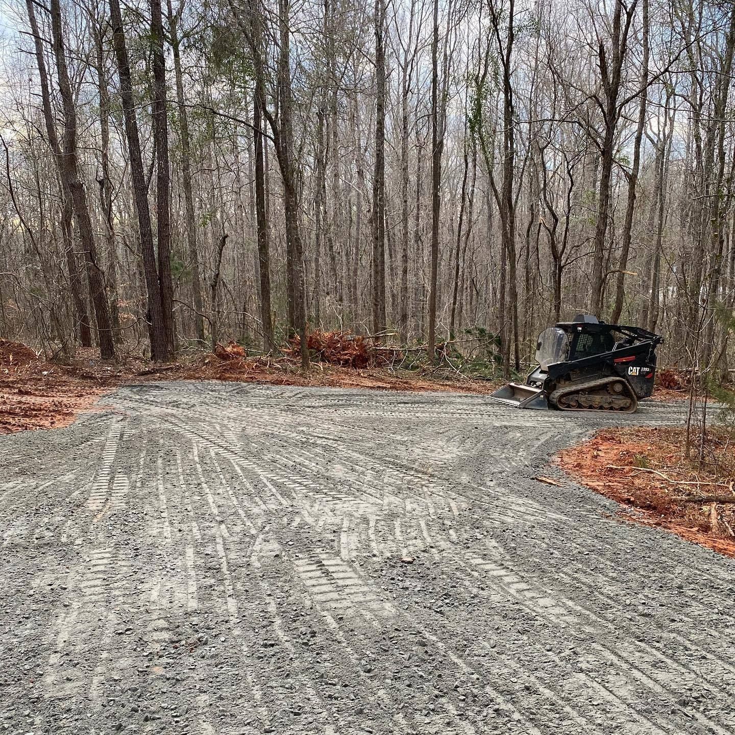 Gravel road with a skid steer in a wooded area, likely under construction.