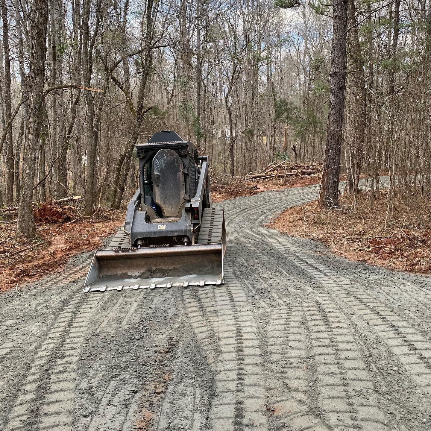 Skid steer on a gravel road through a wooded area. The machine is preparing the path.