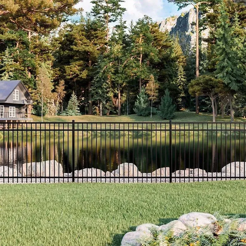 Black metal fence around a pond, with trees, rocks, and a small house in a green wooded landscape.