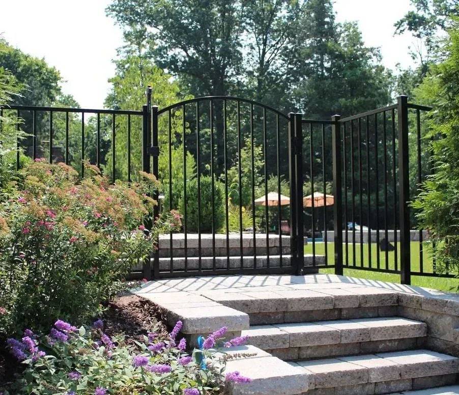 Stone steps lead to a black iron gate in a landscaped garden with flowers and trees.