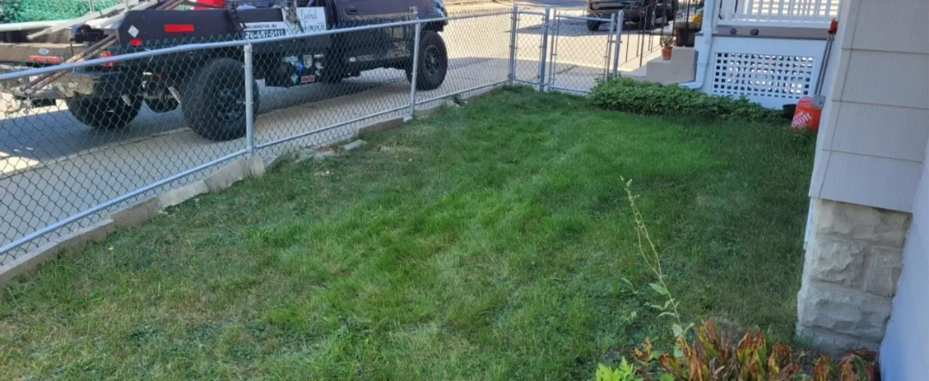 Grassy front yard beside a chain-link fence, with a black pickup truck parked along the street.