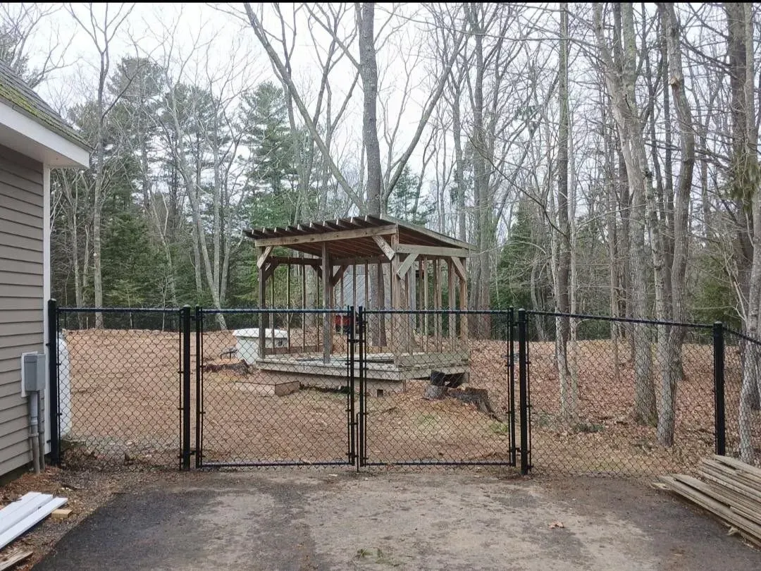 Backyard with chain-link fence and pavilion under construction among leafless trees