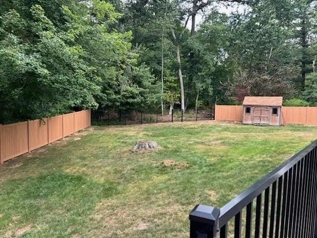Backyard with green lawn, wooden fence, trees, and a small shed