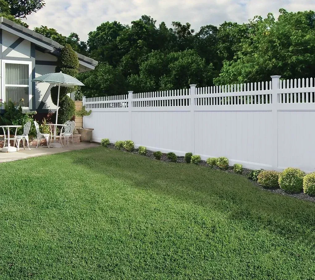 Backyard with green lawn, white fence, and a house patio beside shrubs and trees