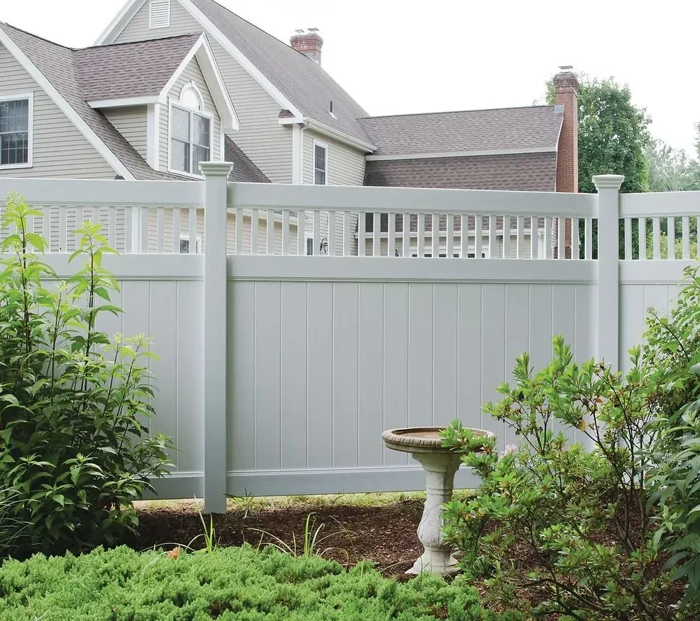 Backyard fence with house and shrubs, featuring a small birdbath in the foreground