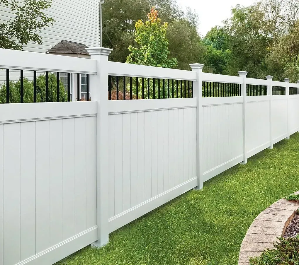 White vinyl privacy fence lining a green lawn with black rail accents and stone edging