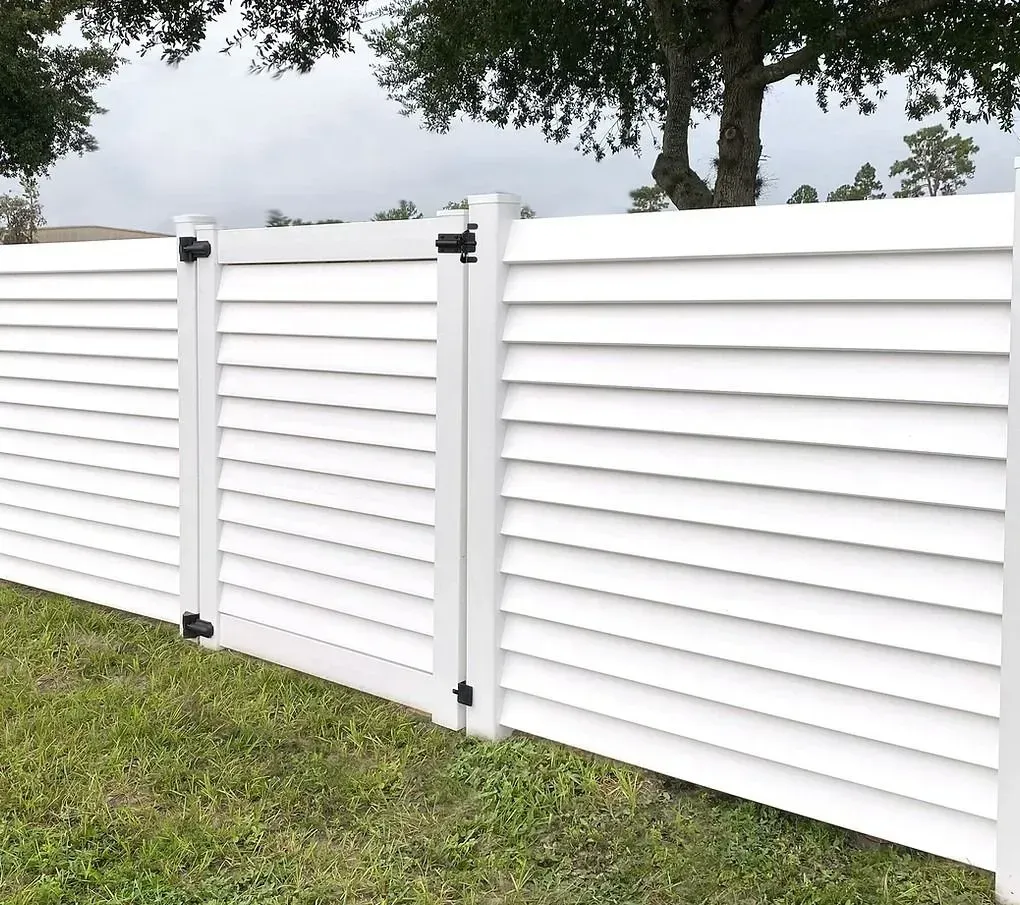 White louvered fence panels in a grassy yard with trees behind them