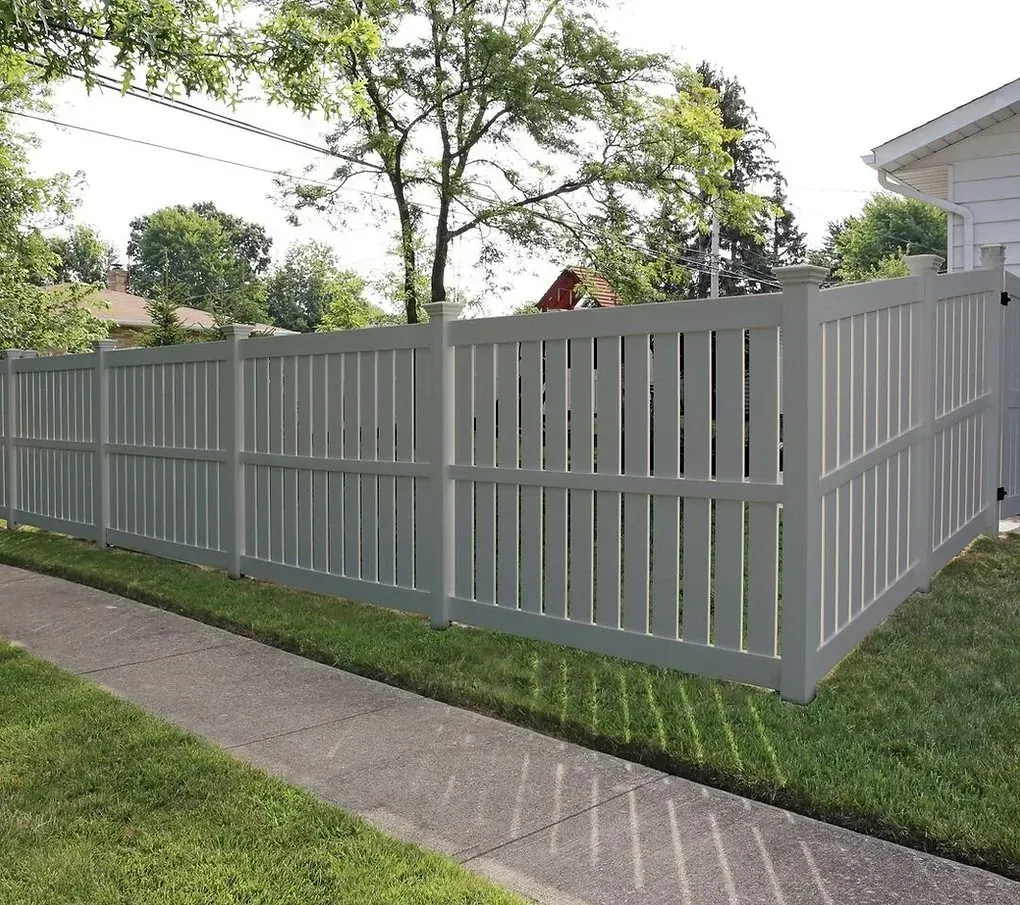 Gray vinyl privacy fence along a sidewalk beside a grassy yard and house