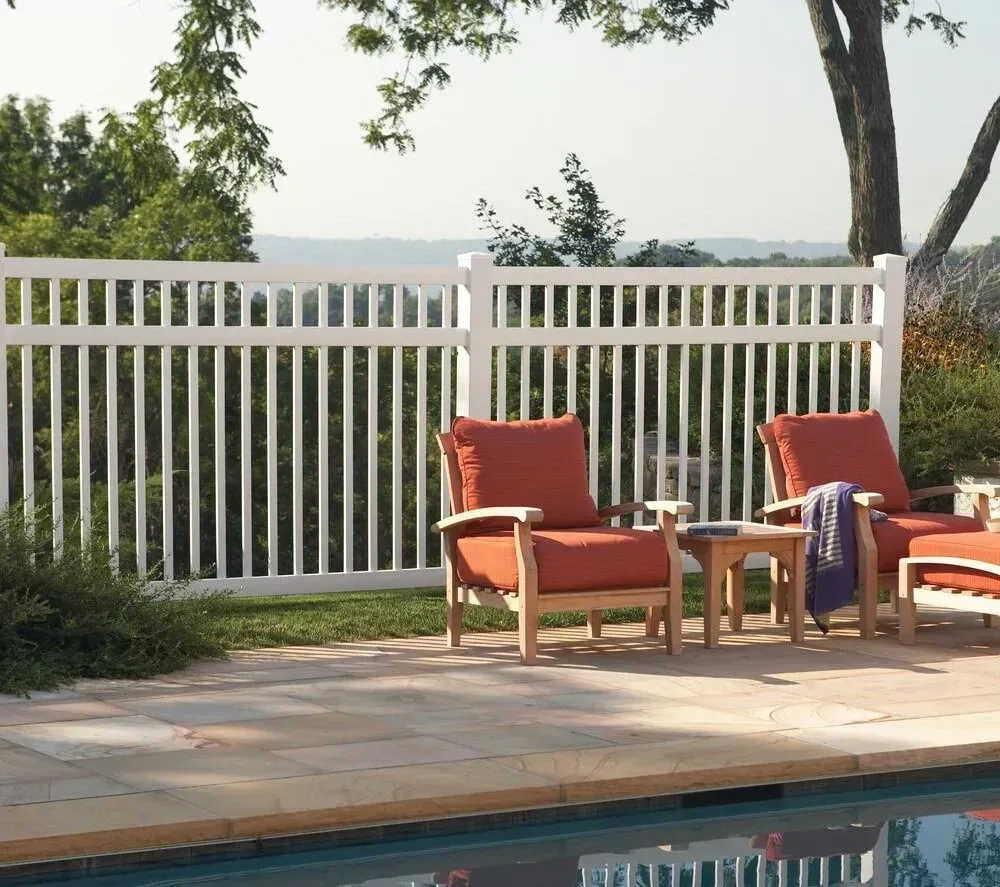 Patio with orange lounge chairs beside a pool, white fence, and trees overlooking water