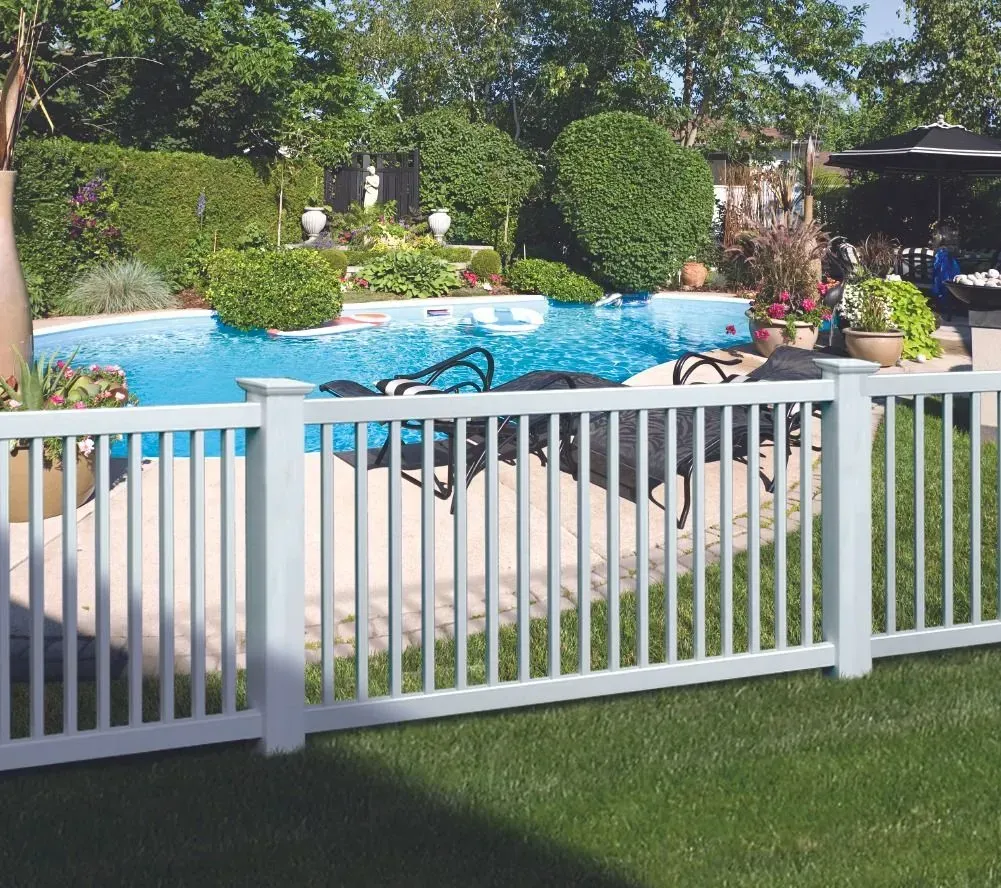 Backyard pool with white fence, blue water, lounge chairs, and trimmed bushes under sunny skies