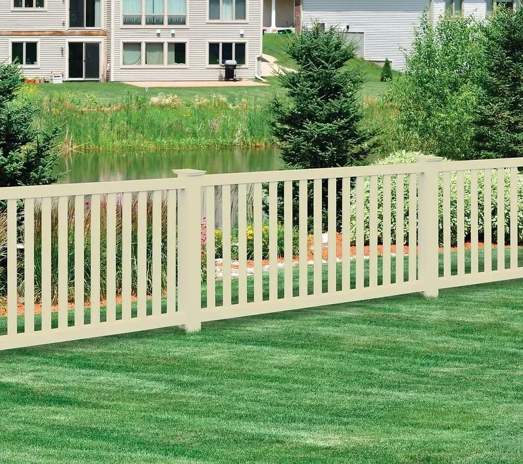 Cream-colored fence along a green lawn beside a pond with shrubs and apartment buildings in the background