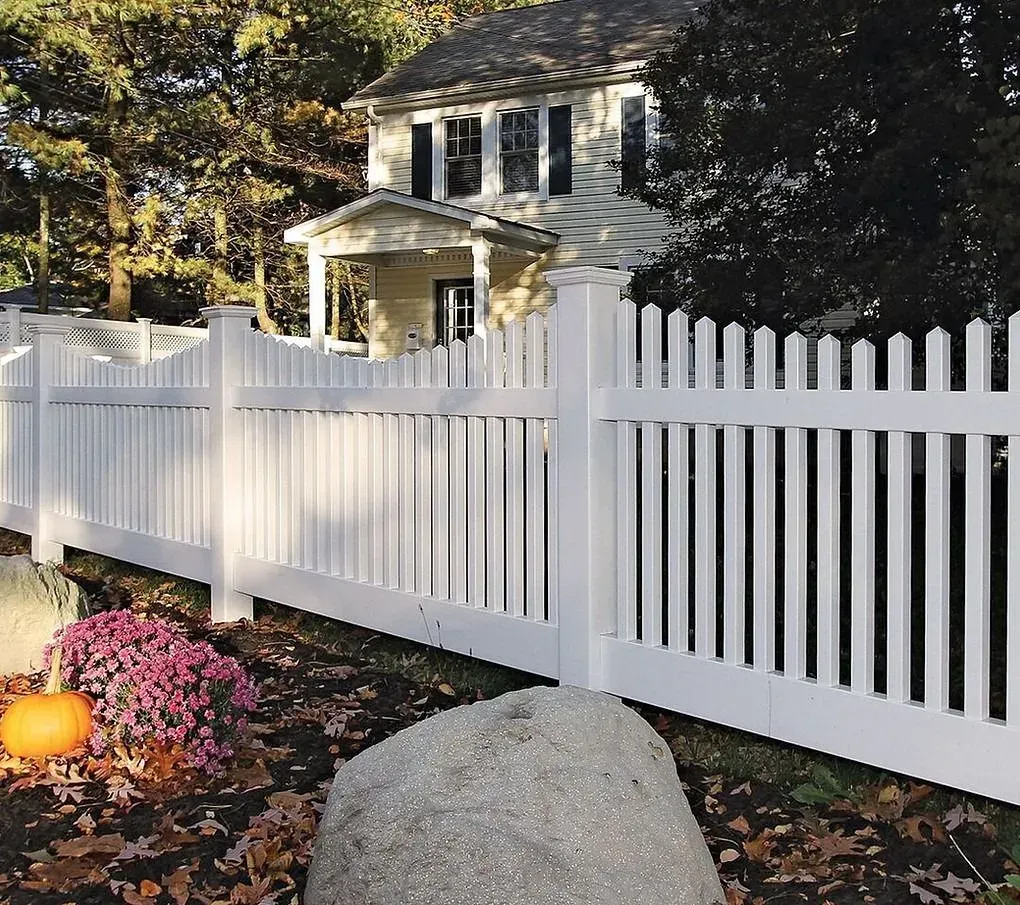 White picket fence in front of a two-story house with autumn leaves, pumpkins, and a large rock in the foreground