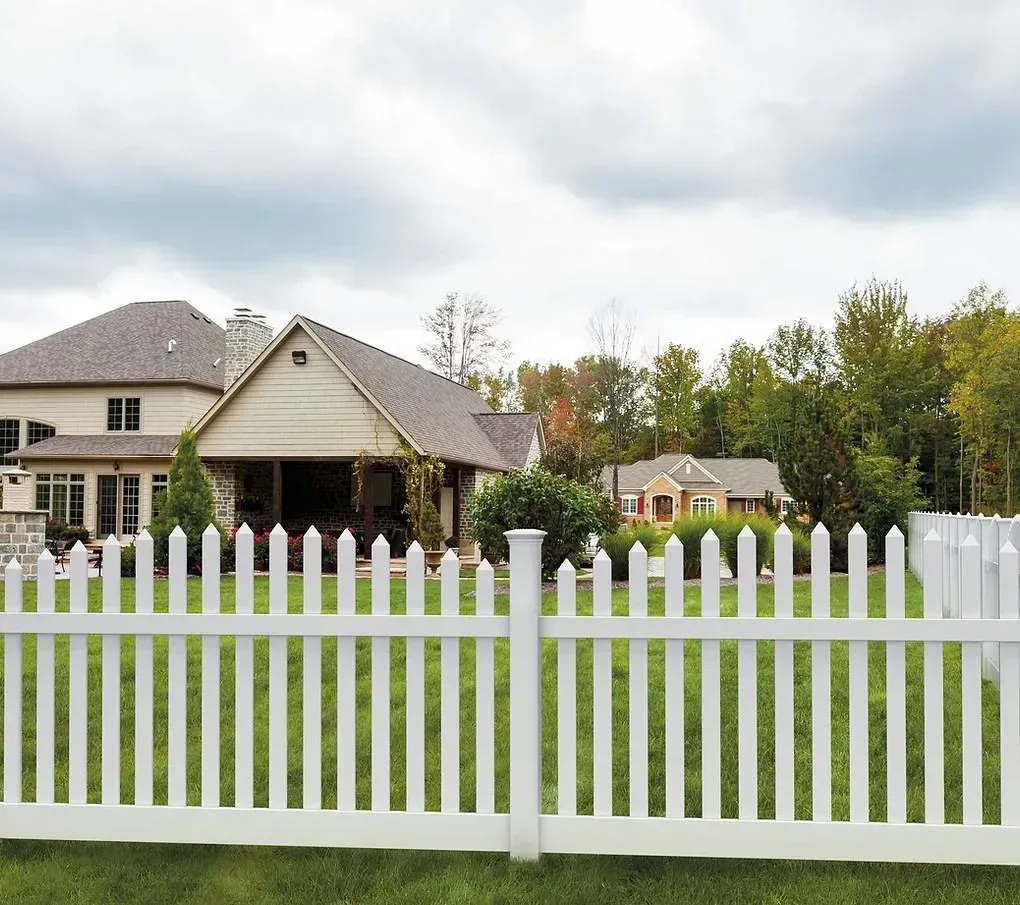 White picket fence in front of a suburban house and green lawn under cloudy sky