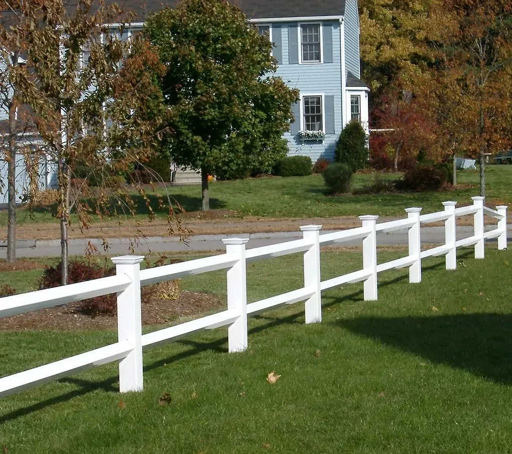 White wooden fence along a green lawn in a suburban neighborhood with a blue house in the background