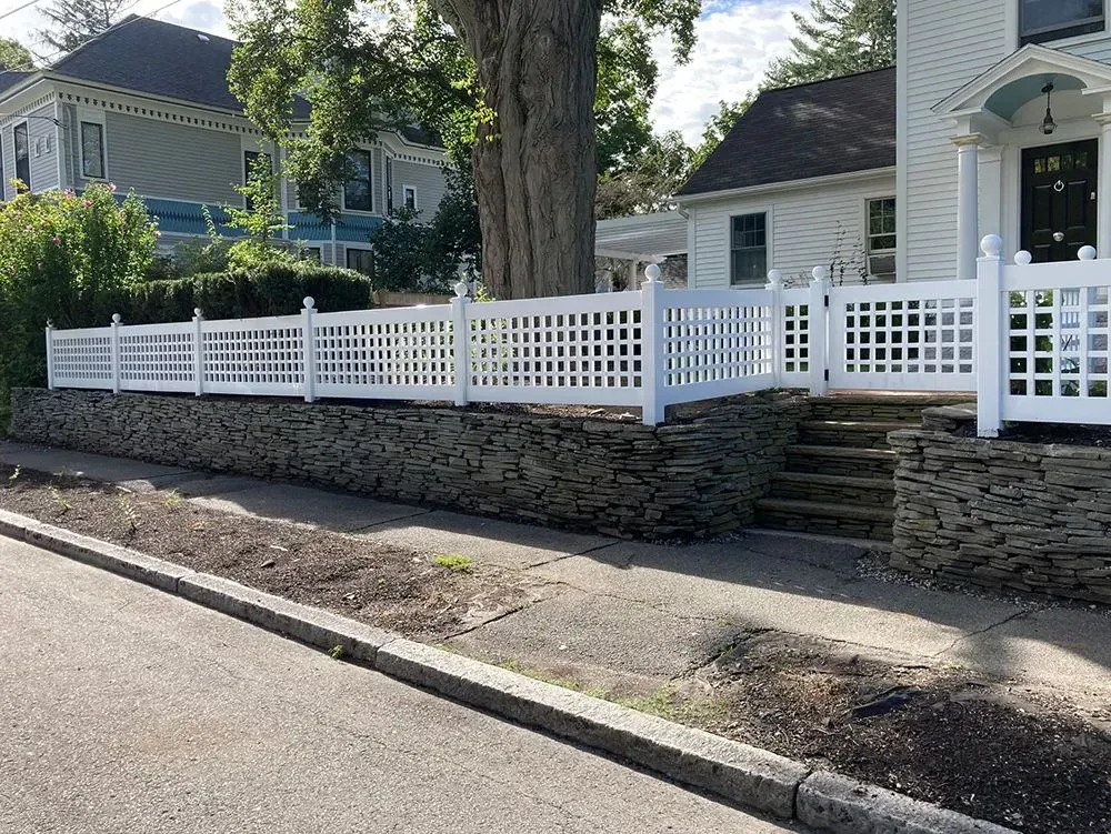 White picket fence atop a stone wall along a tree-lined residential street with houses and front steps