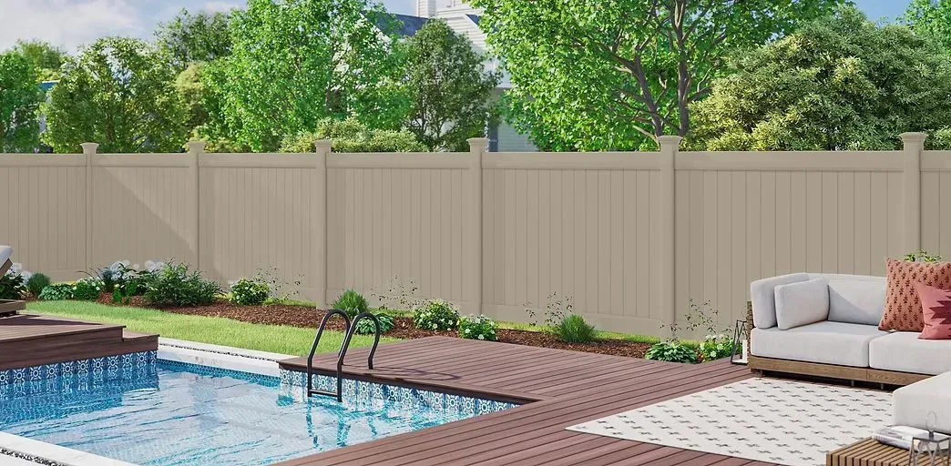Backyard pool beside brick patio, beige privacy fence, and cushioned lounge chair with umbrella shrubbery.