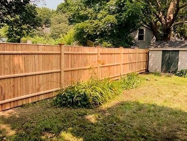 Backyard with a wooden privacy fence, grassy yard, and shed under trees on a sunny day