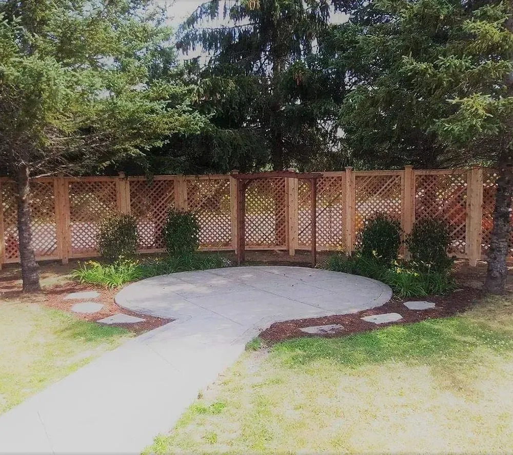 Backyard patio with a circular concrete pad, stone path, and wooden lattice fence surrounded by trees