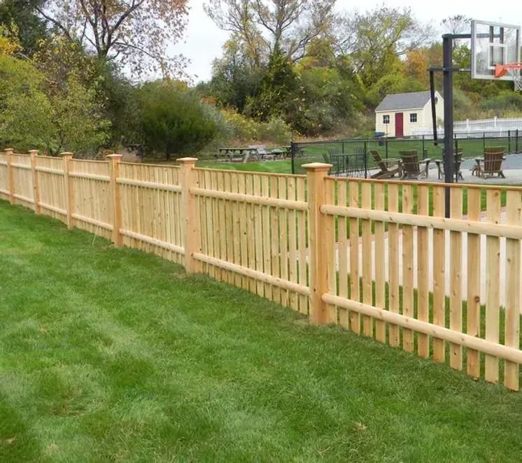 Wooden fence along a grassy yard near a basketball court and small house
