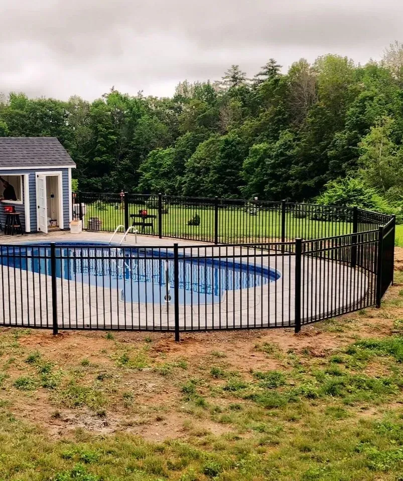 Backyard with fenced-in above-ground pool beside a small shed and grassy yard, surrounded by trees