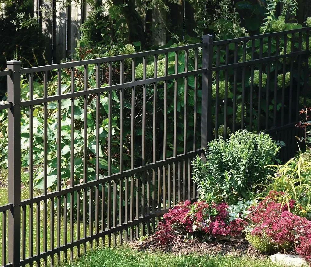 Black metal garden fence beside lush greenery and pink flowers in sunlight