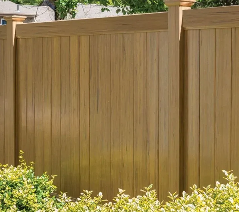 Wooden privacy fence with tan panels and green shrubs in front