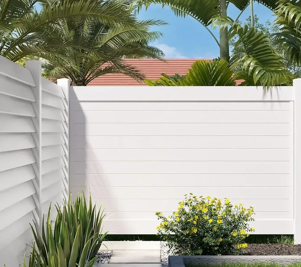 White privacy fence with palm trees, green plants, and a small yellow-flowering shrub in a sunny yard